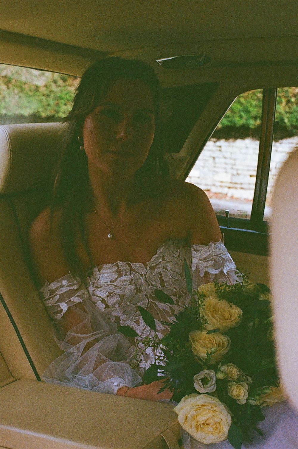 A vintage-style wedding photo showing a bride with yellow roses in the backseat of a classic car.
