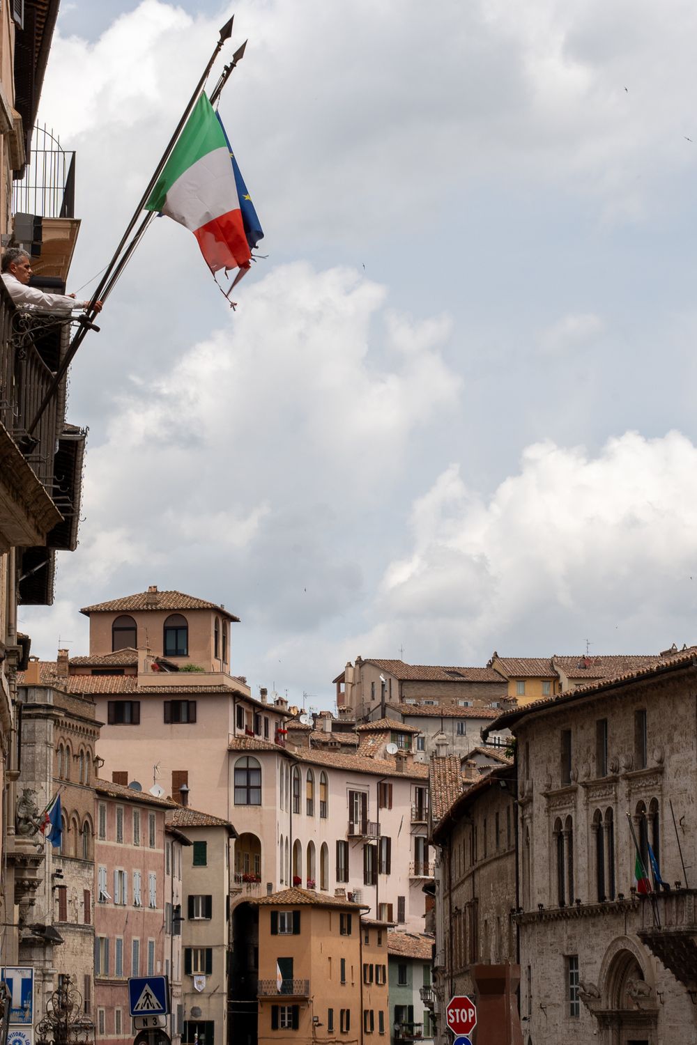 Italian flag waves above traditional architecture in a historic town center.
