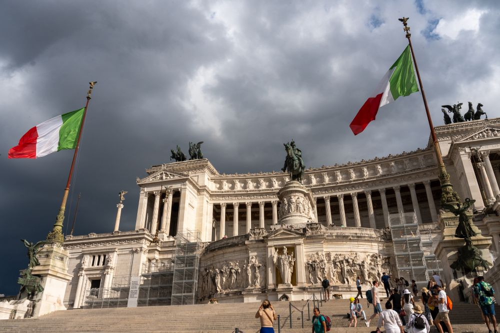 Monumento Nazionale a Vittorio Emanuele II in Rome with Italian flags under stormy skies.