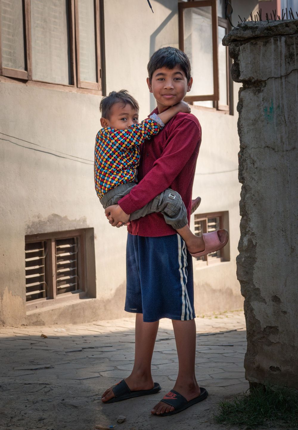 Siblings pose together in traditional clothing against building wall in Nepal.