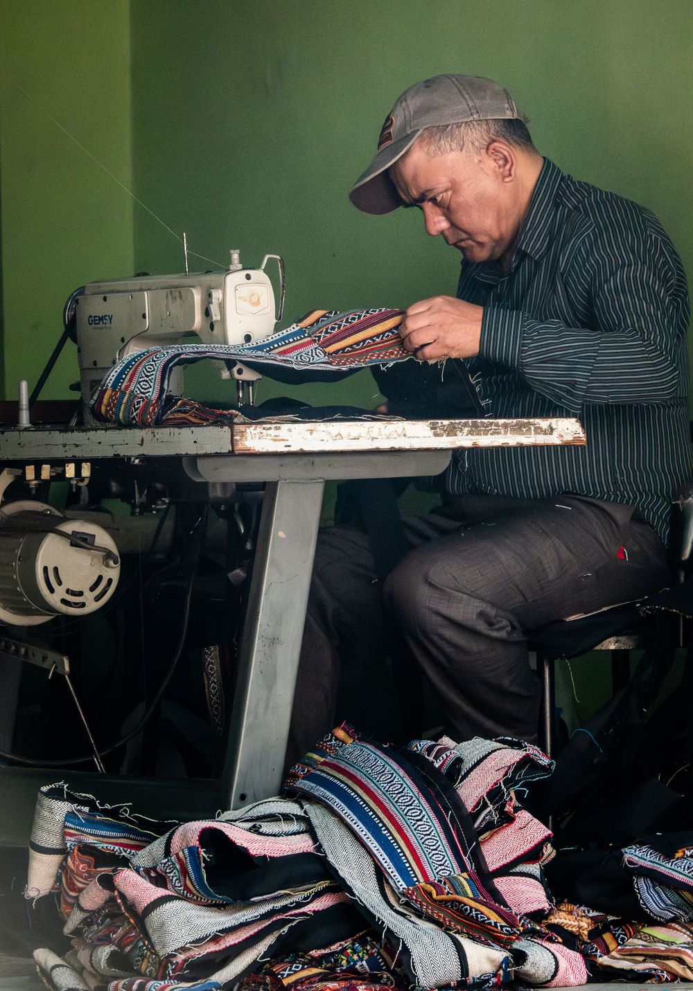 Craftsman working on a sewing machine with colorful fabric pieces in a workshop.