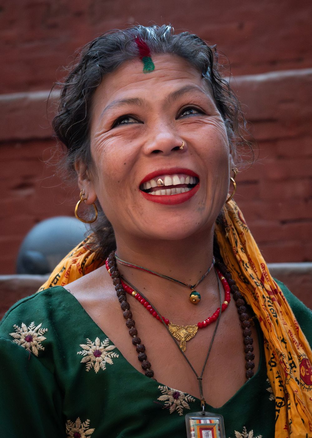 Traditional Nepali woman wearing ornate jewelry and green dress with golden embroidery.