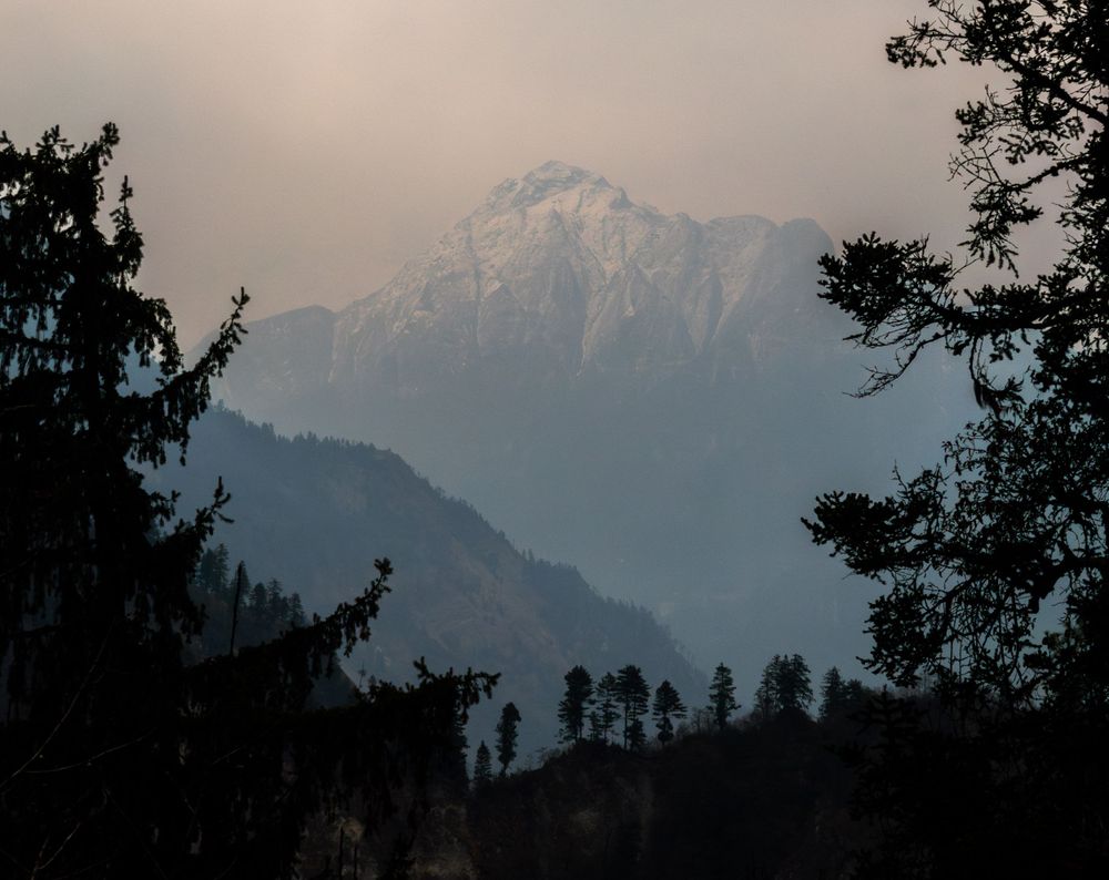 Silhouette of mountain peak through trees at sunset in Nepal.