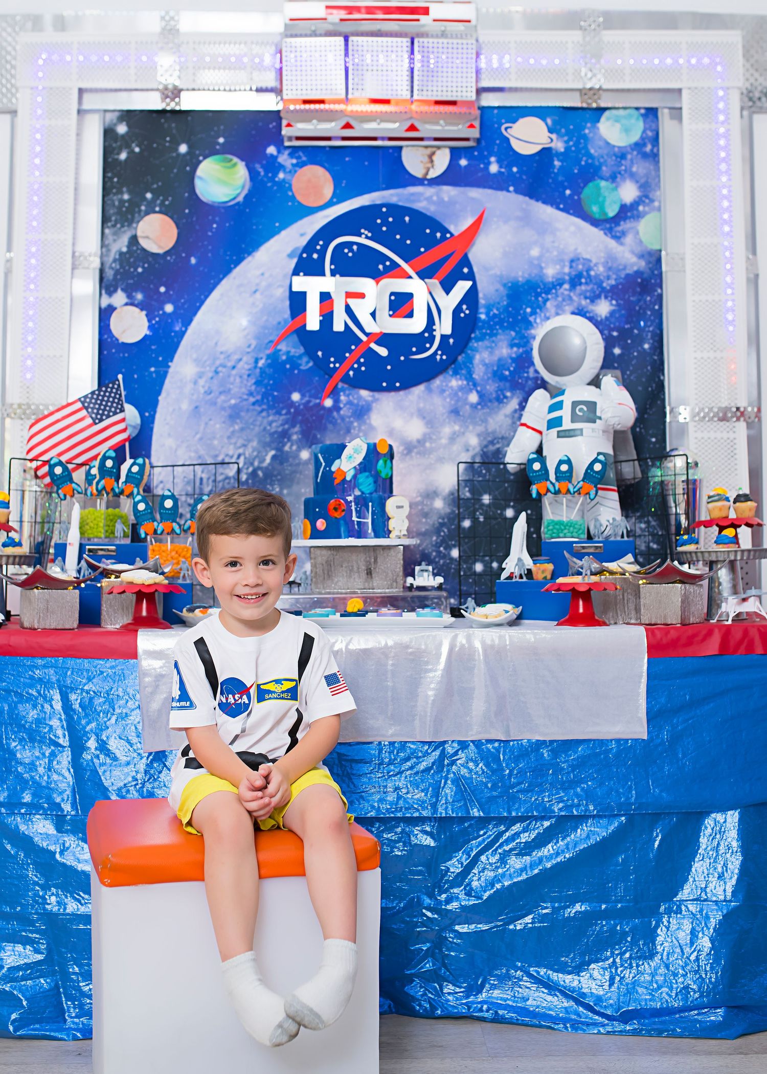 Custom NASA-inspired party backdrop with TROY logo, astronaut figure, and space-themed decorations.