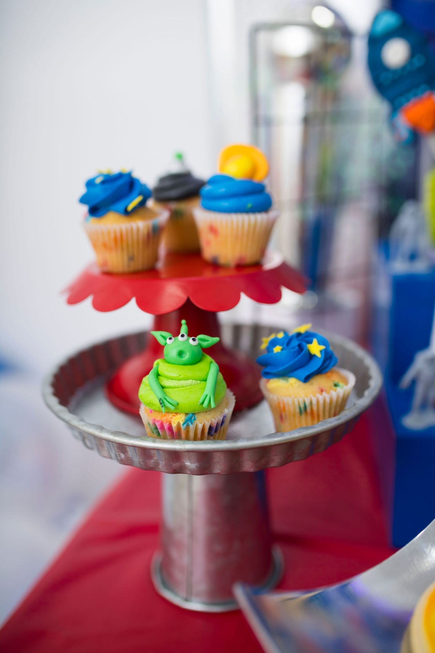 Space-themed cupcakes with blue frosting and alien designs on tiered display stand.
