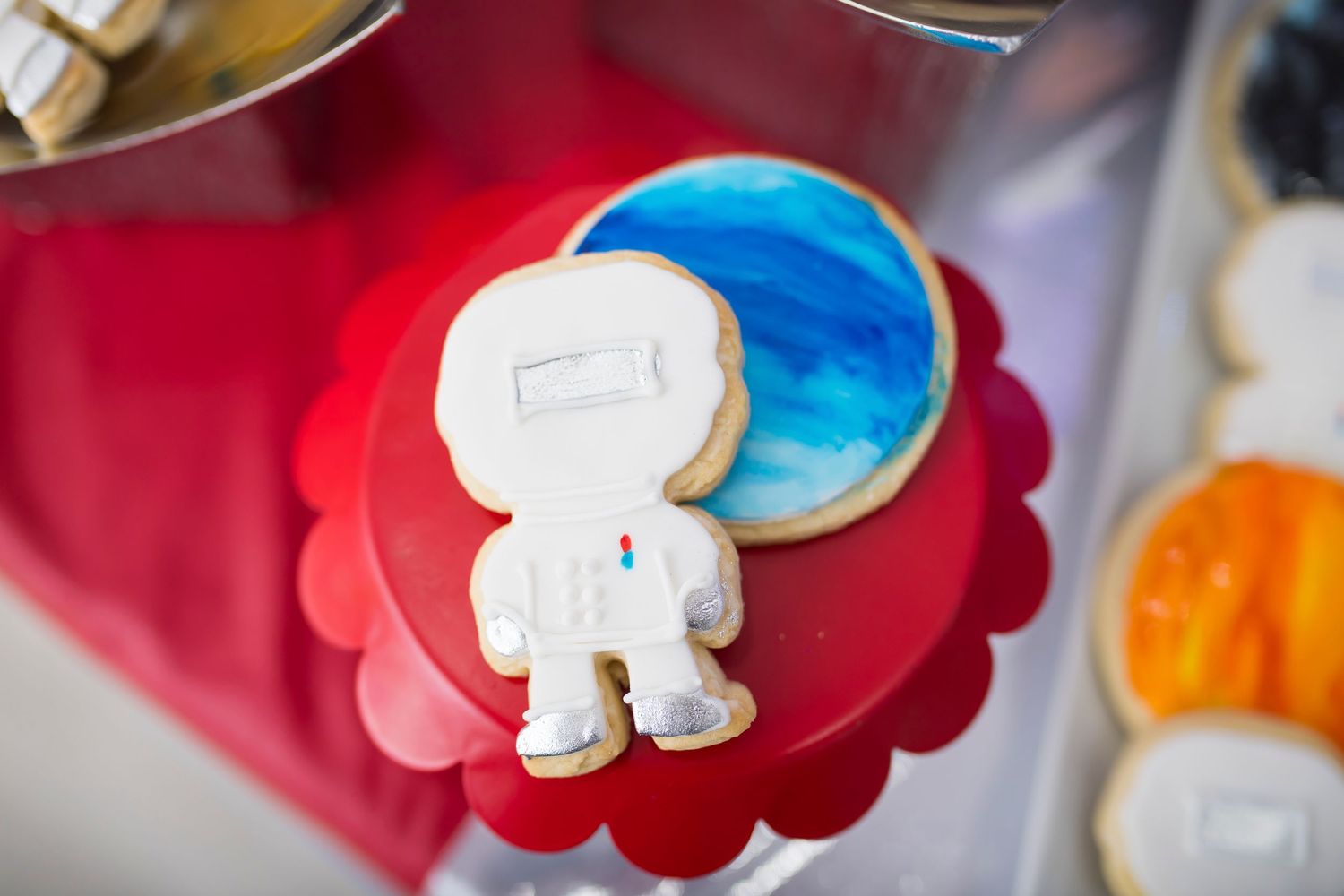 White astronaut cookie on red scalloped plate with blue cookies in background.