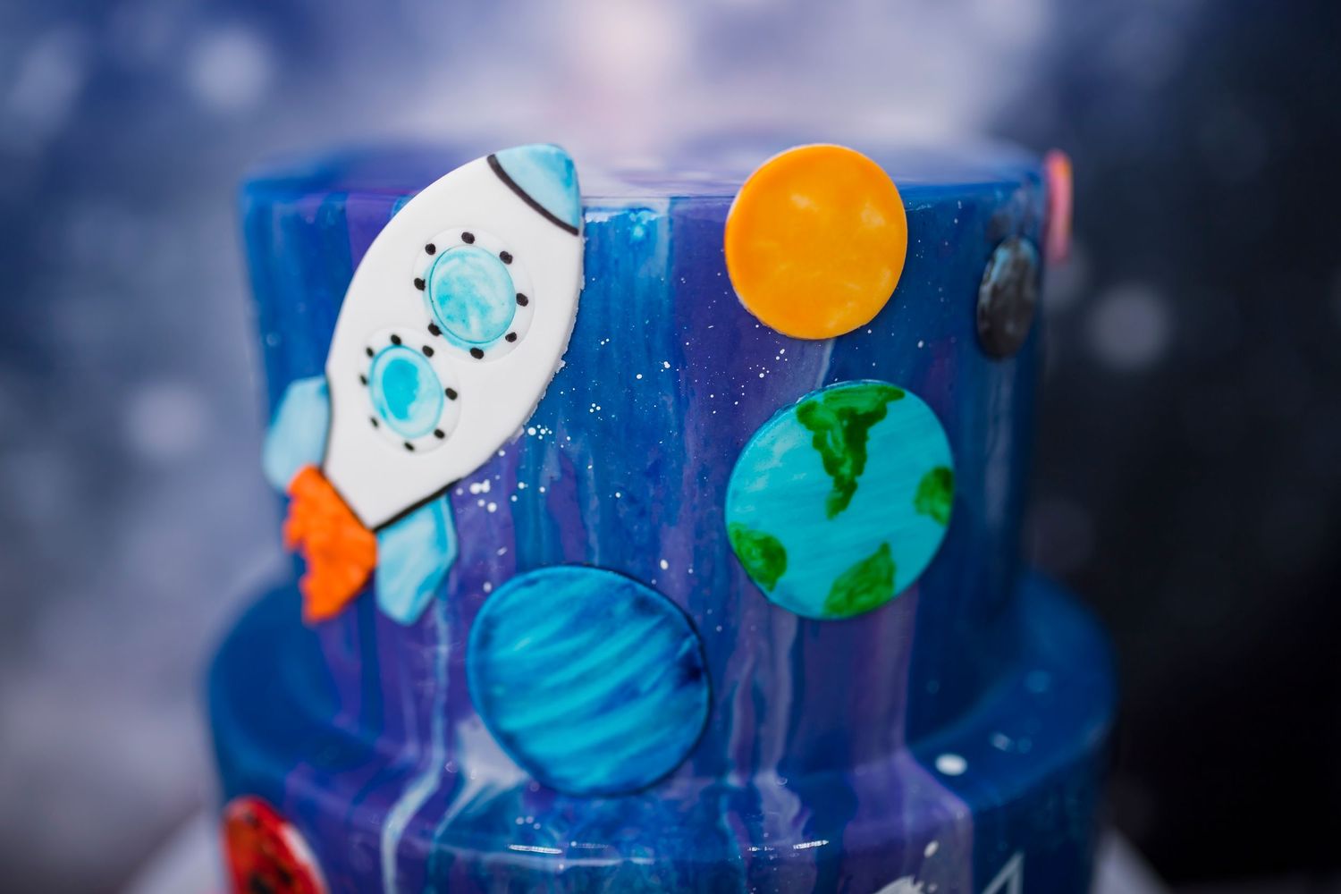 Close-up of a space-themed cake featuring planets, a rocket ship, and Earth against a dark blue galaxy background.