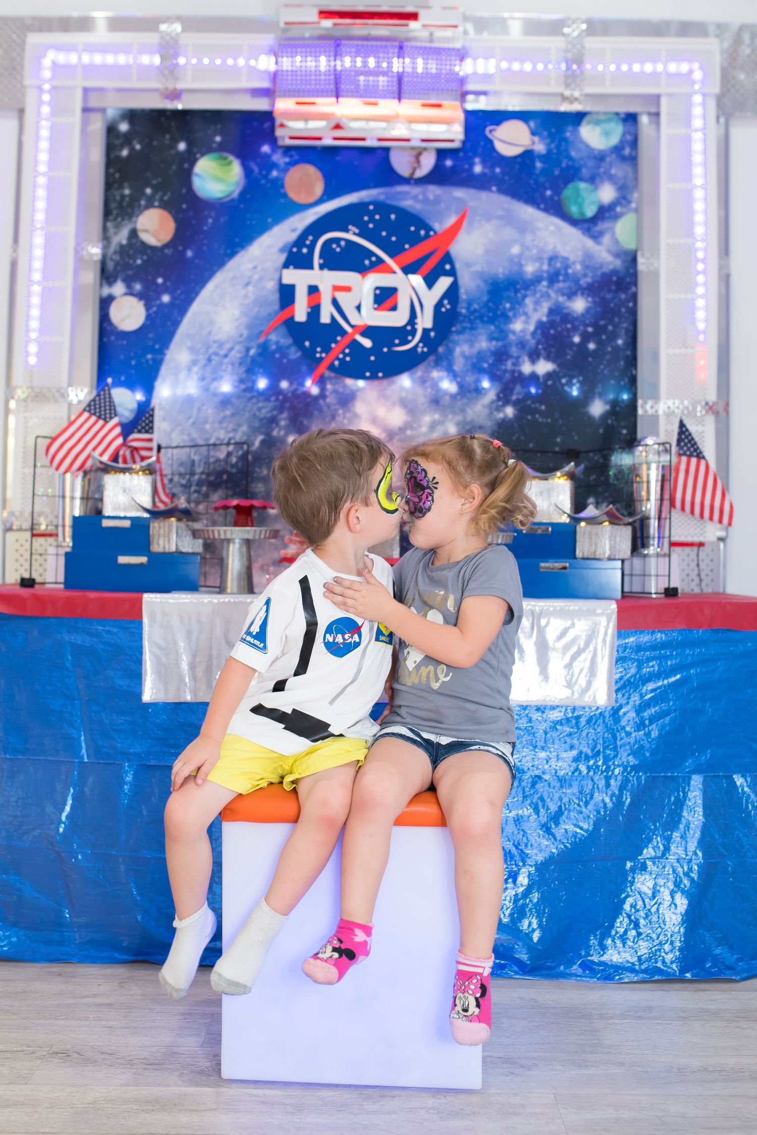 Space-themed party setup with custom logo backdrop, American flags and blue table coverings.
