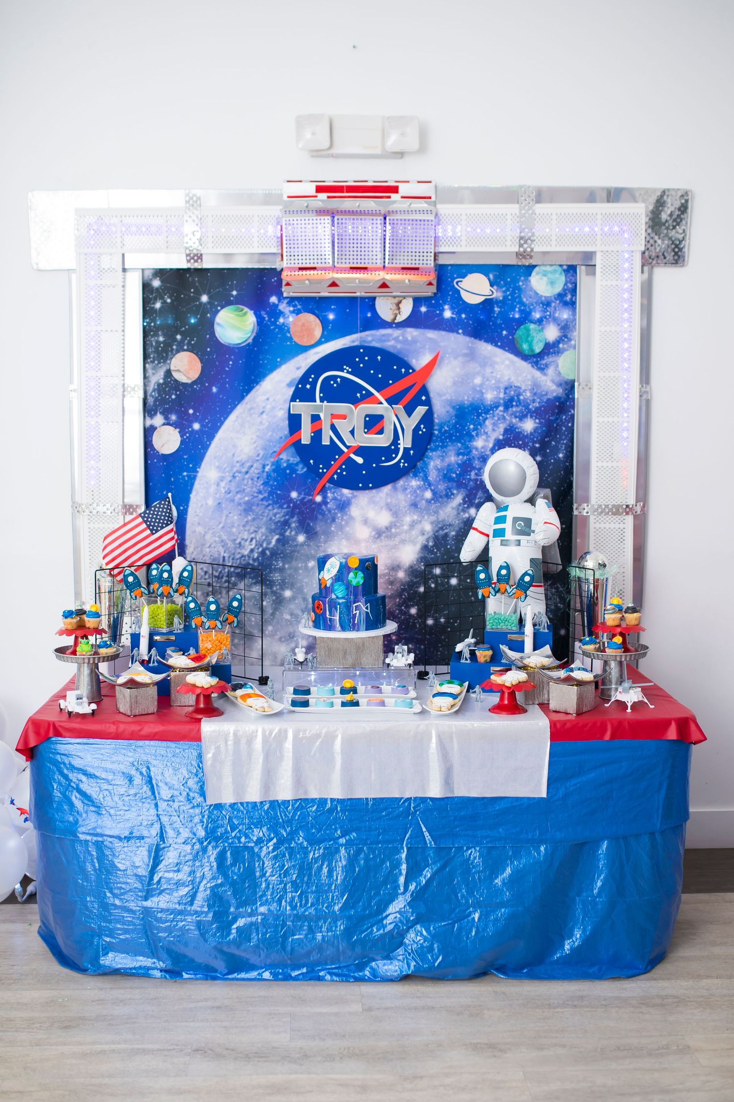 NASA themed party display with space backdrop and themed decorations on blue tablecloth.