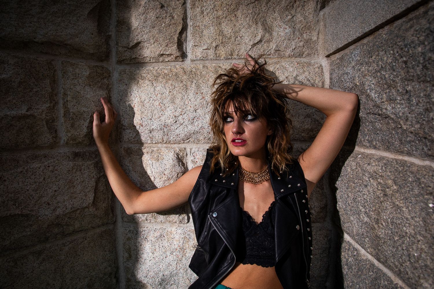 Fashion portrait against stone wall featuring edgy punk rock style and dramatic lighting.