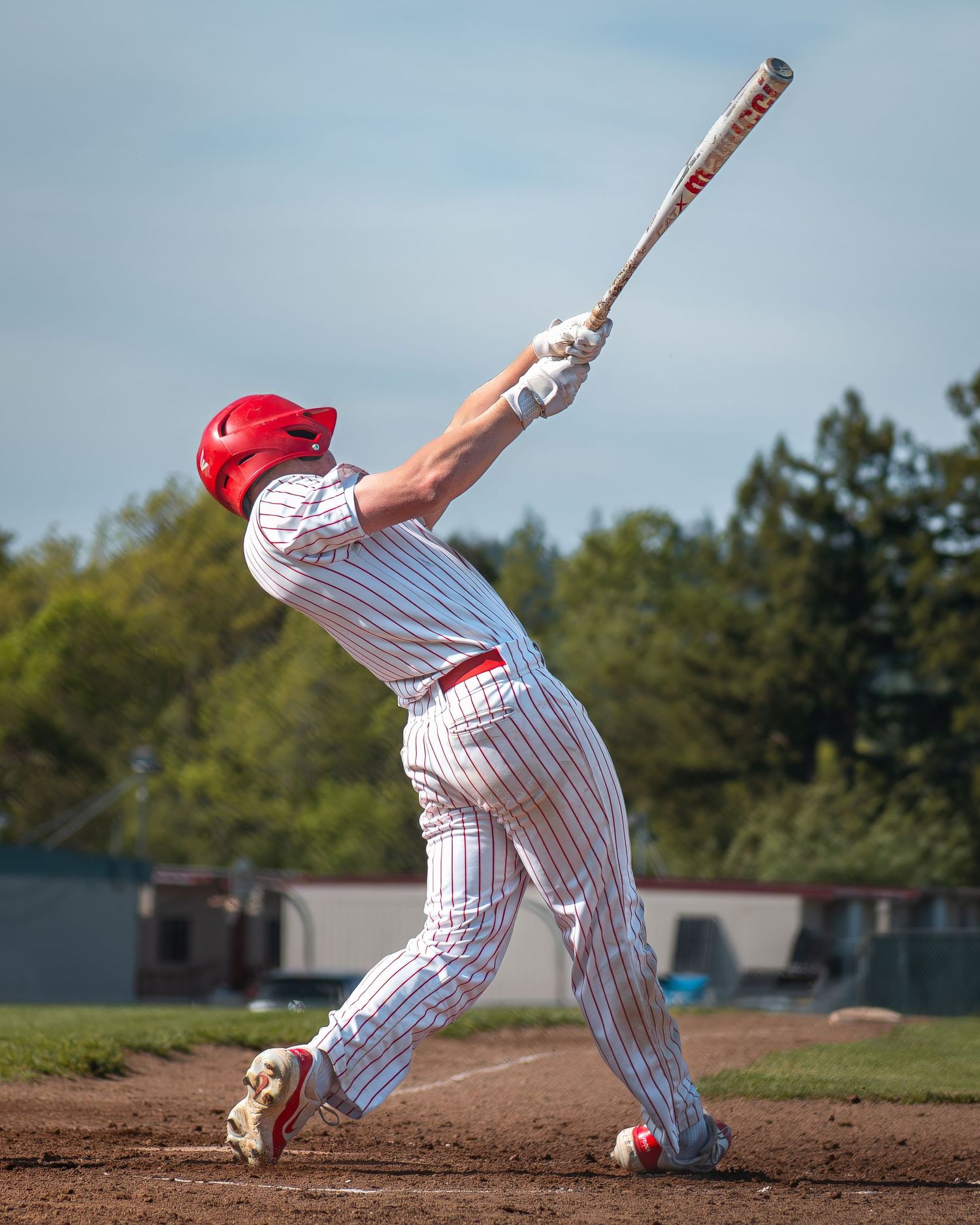 Baseball player in pinstripe uniform swinging bat during game against blue sky backdrop.