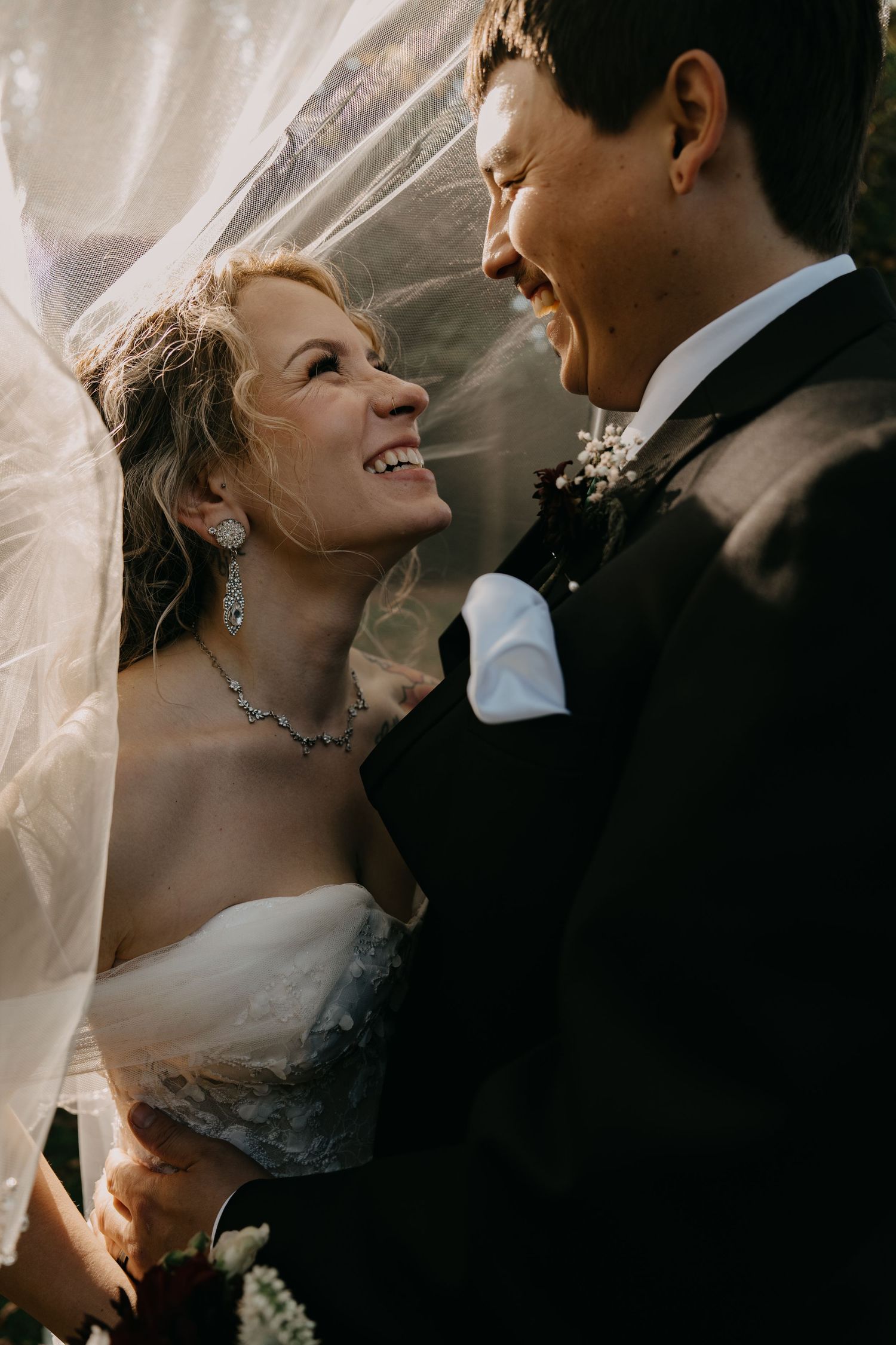 An intimate candid moment between newlyweds sharing joyful laughter under a bridal veil.