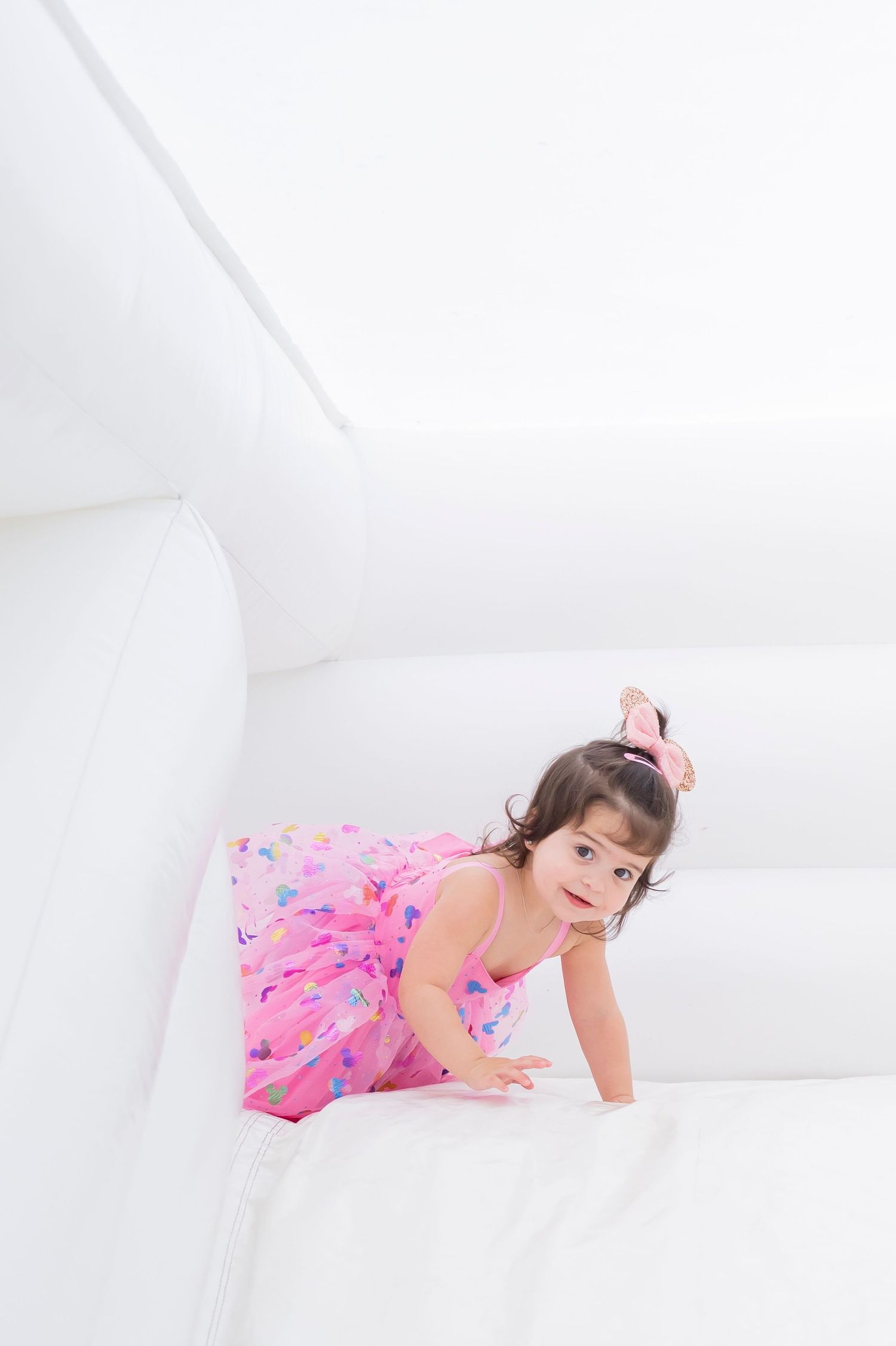 Child in pink dress playing inside white bounce house.