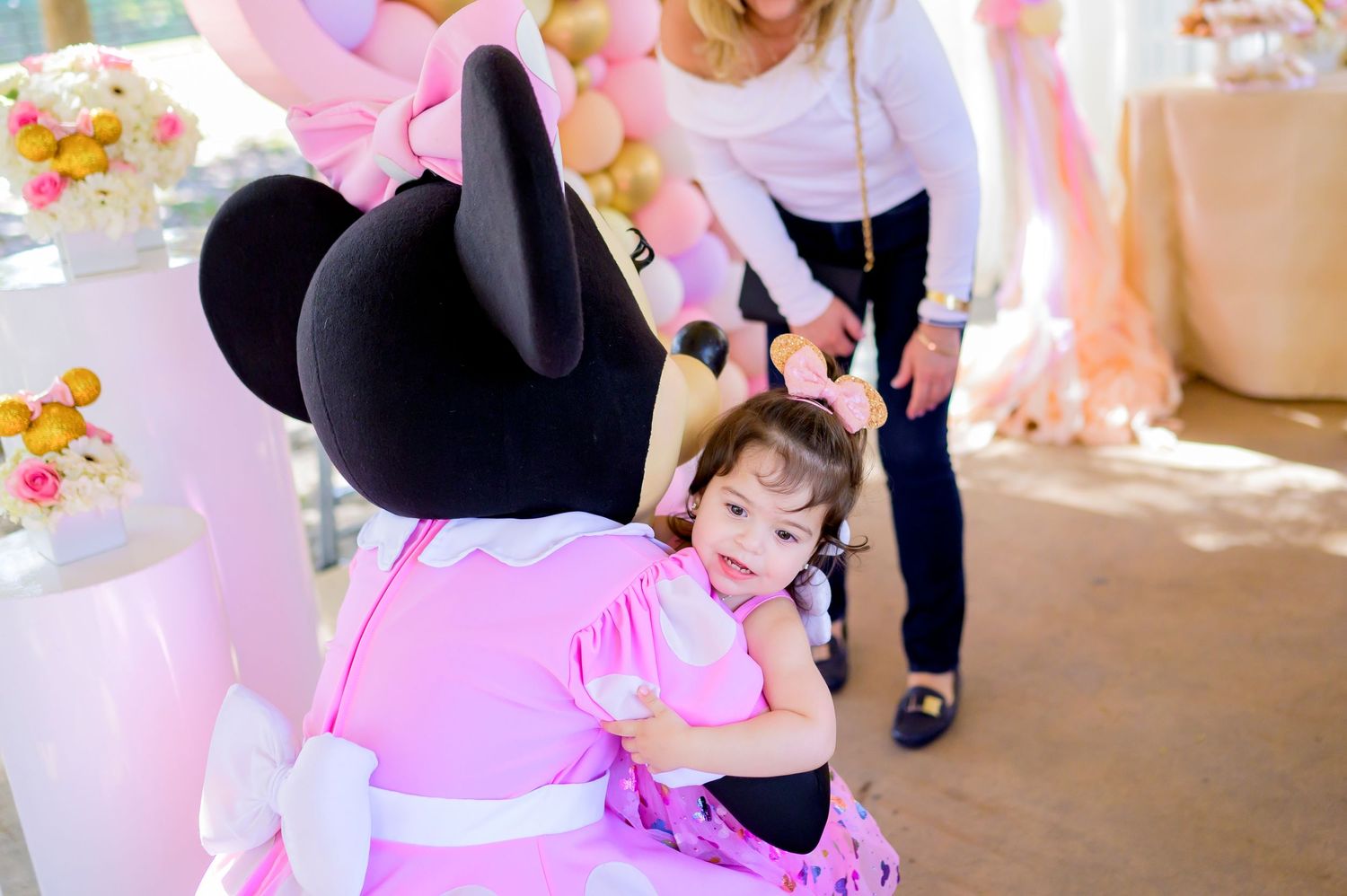Minnie Mouse character gives a warm hug during a pink-themed celebration.