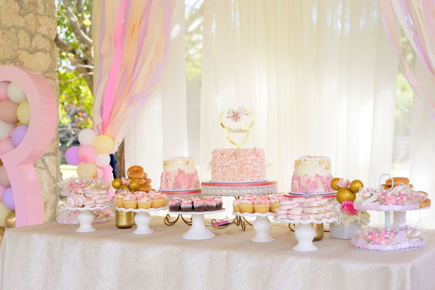 Elegant dessert table with pink and white decorations featuring cakes and party treats.