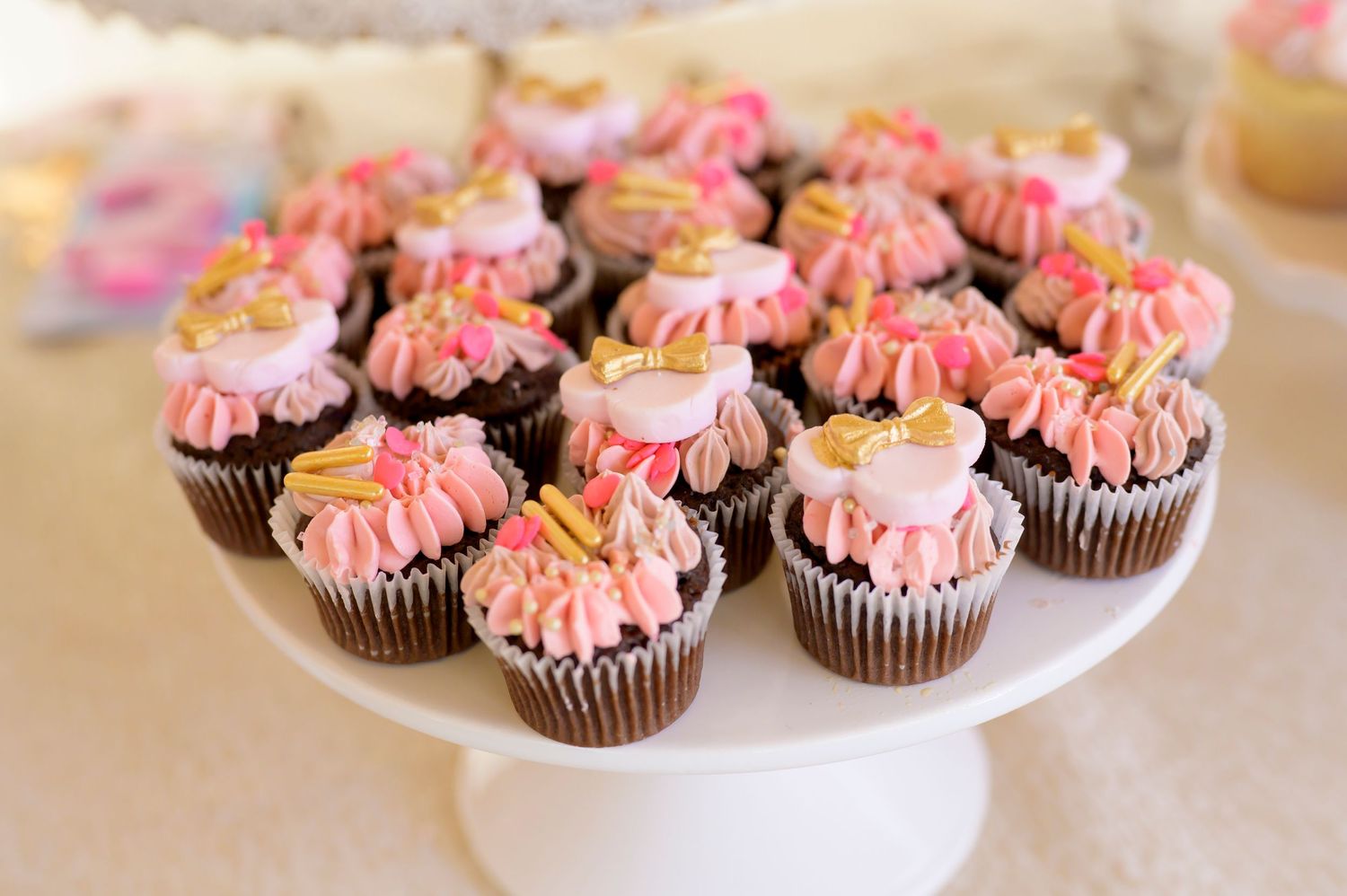 Chocolate cupcakes with pink frosting swirls displayed on white cake stand.