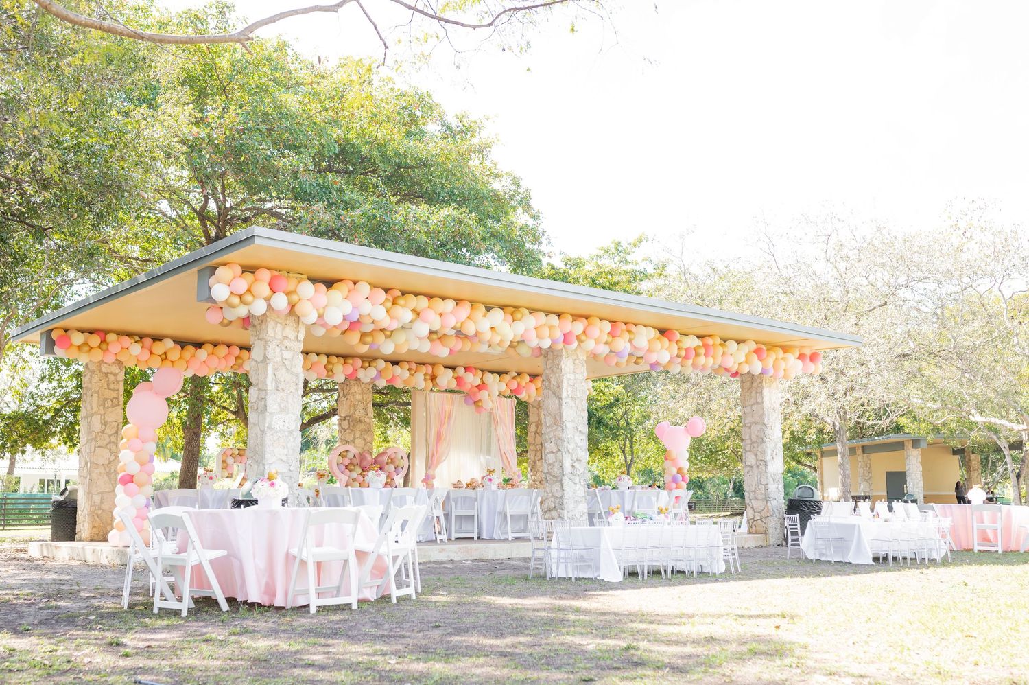 Covered outdoor pavilion decorated with pink and gold balloons for an elegant party setting.