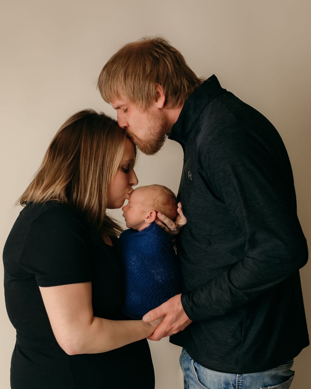 Intimate family moment showing tender affection with newborn baby in dark clothing.