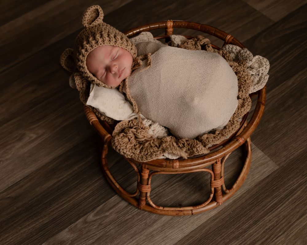 Sleeping newborn in knit bonnet resting peacefully in round woven basket.