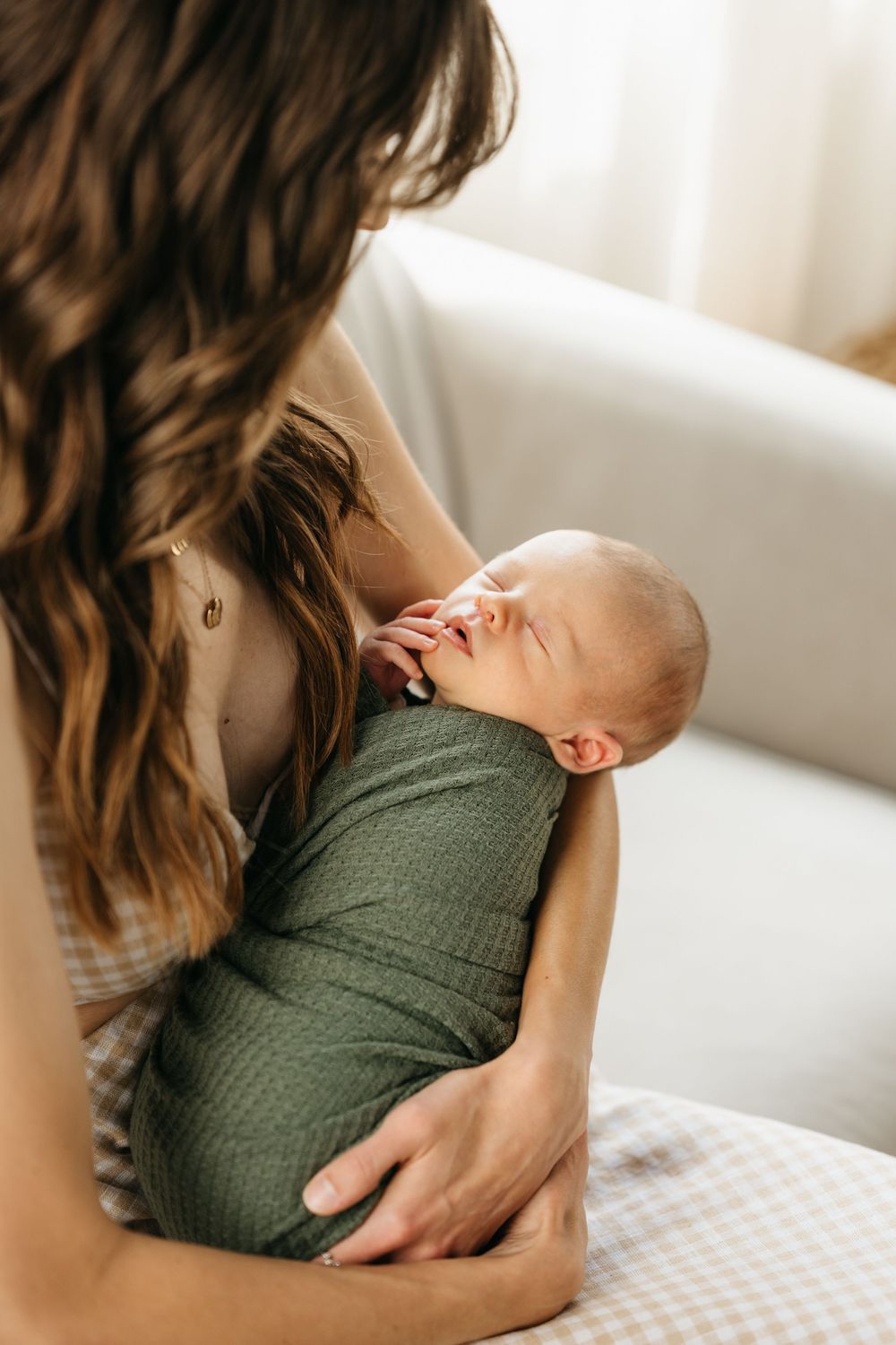 A tender moment between parent and newborn baby in a green swaddle blanket on a white surface.