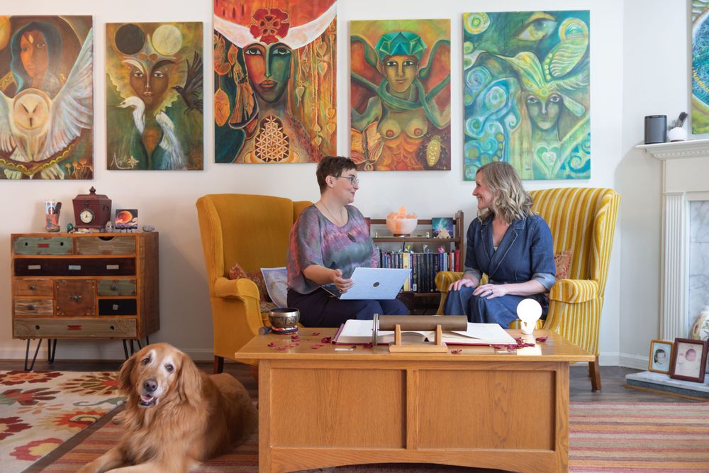 Living room decorated with colorful artwork features two people having coffee on yellow couch with golden retriever nearby.