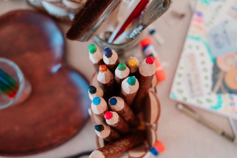 Close-up of colorful pencils in wooden holder with books in background.