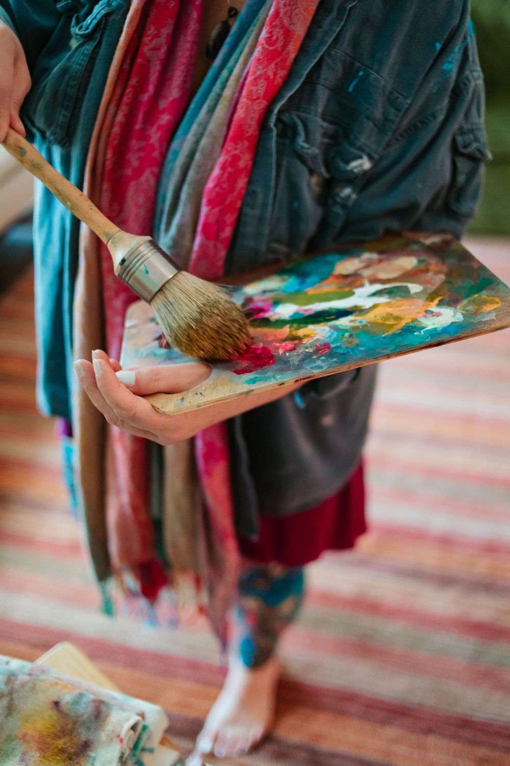 Artist holding paint palette and brush while wearing colorful flowing clothes.