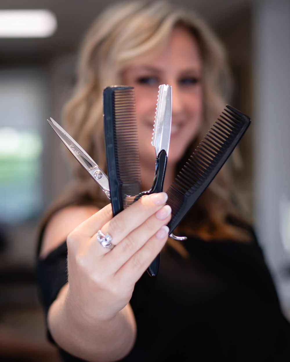 Professional hair styling tools including combs and scissors held up against blurred background.