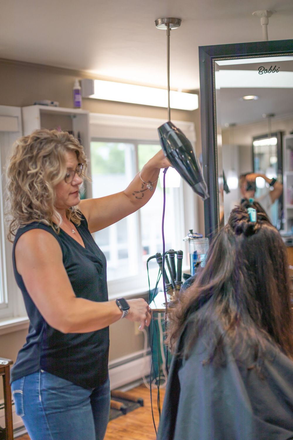 Hair stylist using blow dryer while styling client's dark hair in salon.