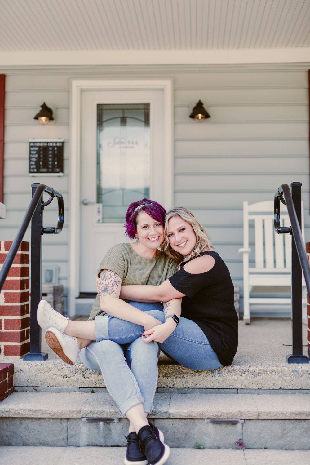 Two people sitting together on front porch steps of white siding building.