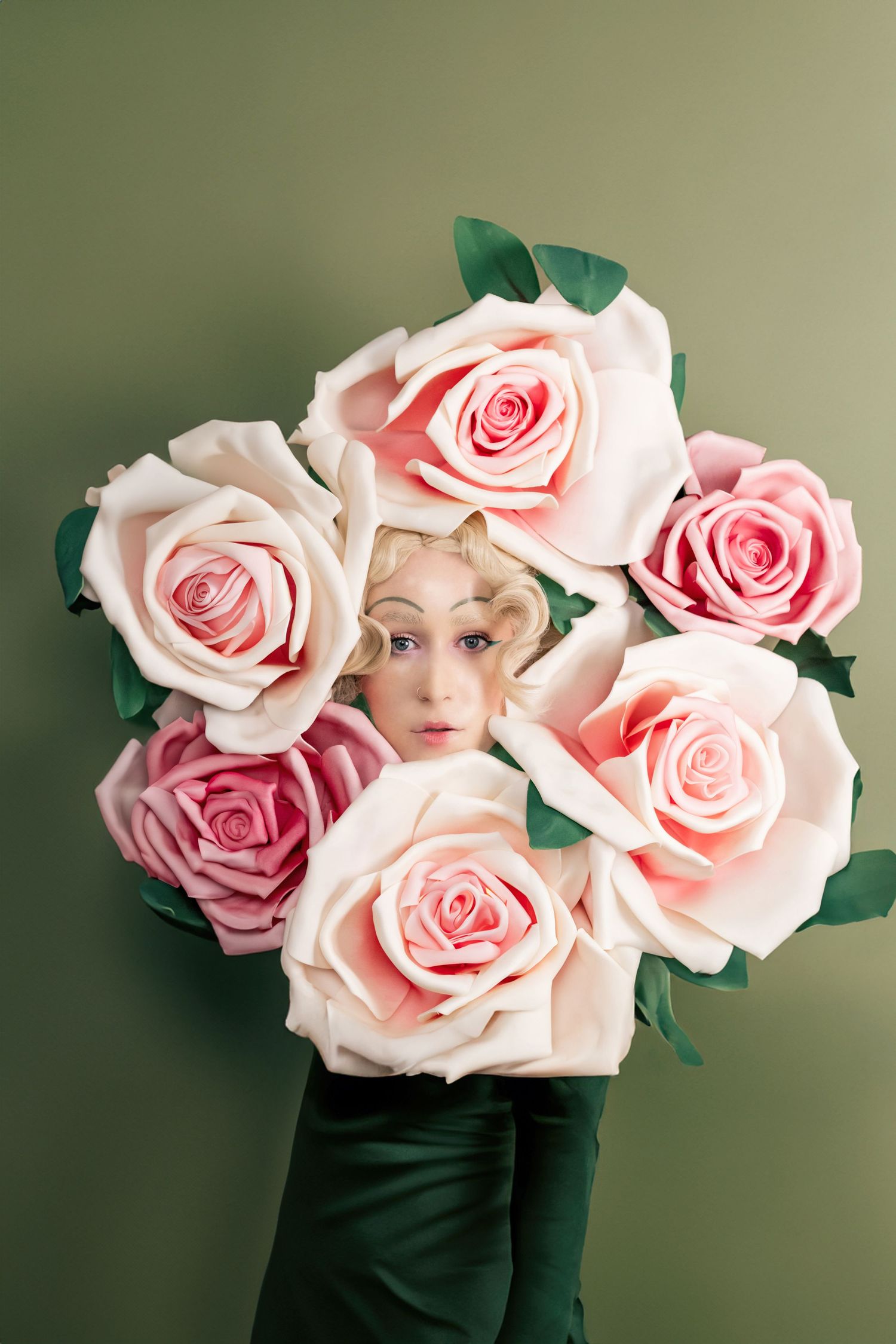 Creative portrait surrounded by delicate pink roses against a soft green background.