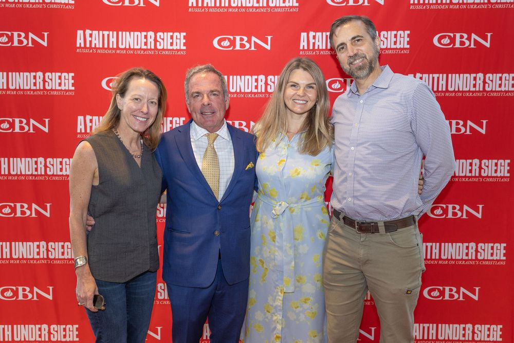Four people pose together at a red CBN media wall wearing business casual attire at what appears to be a formal event.