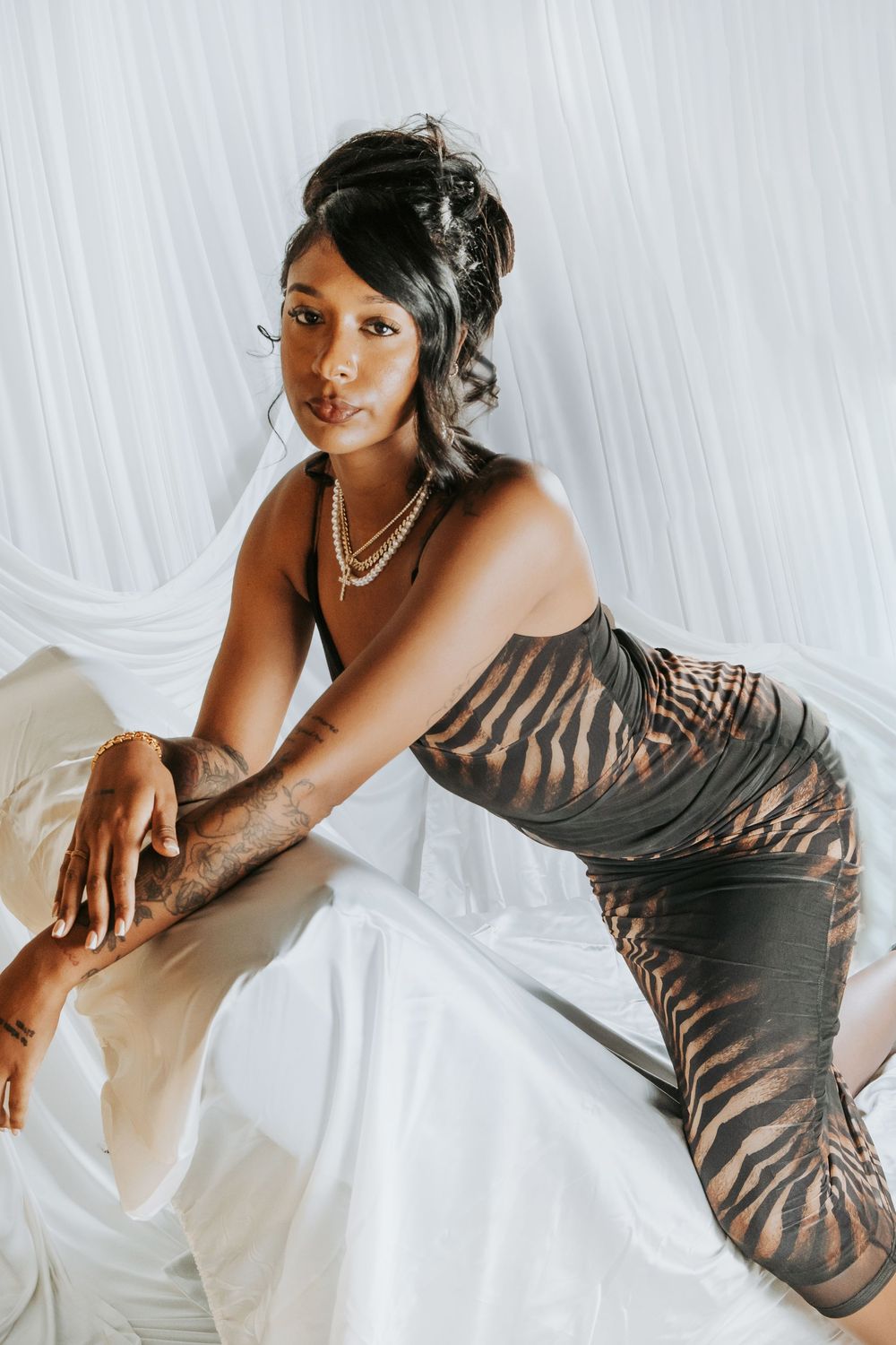 A woman in a zebra-print dress poses gracefully against white draping, wearing pearl necklaces and hair accessories.