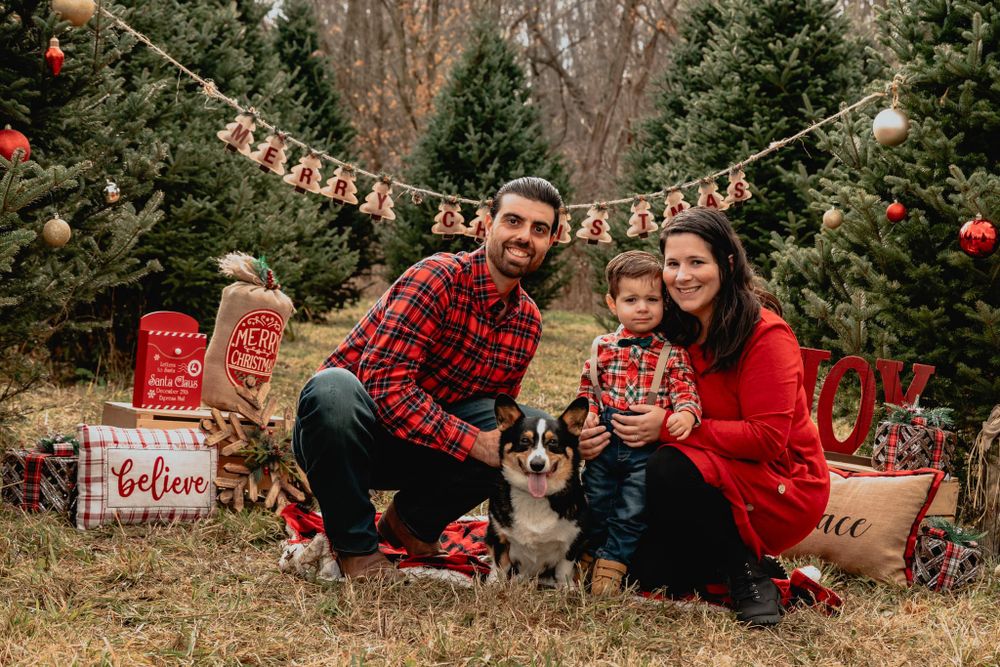 Family holiday photo with couple and dog surrounded by Christmas decorations and presents.