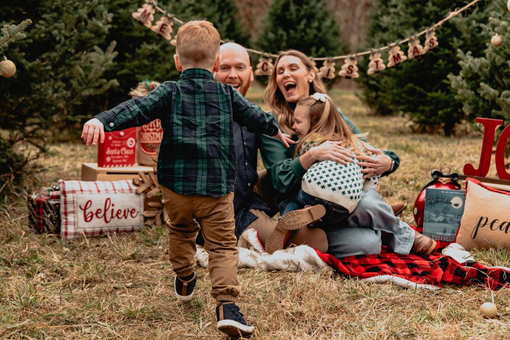 Candid family Christmas photo with child running towards parents and dog on picnic blanket.