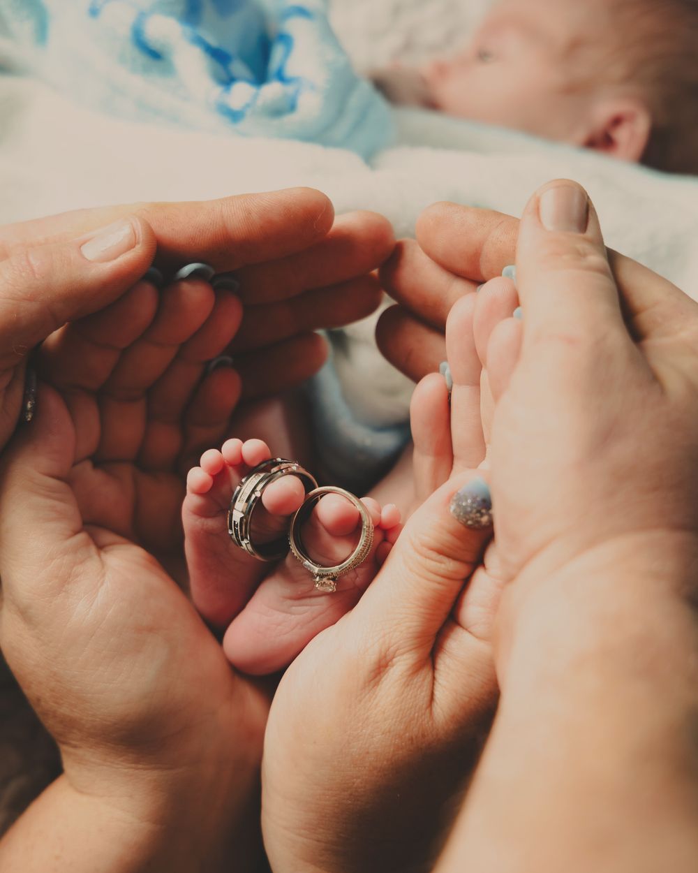 Close up photo of tiny baby feet held in adult hands with wedding rings.