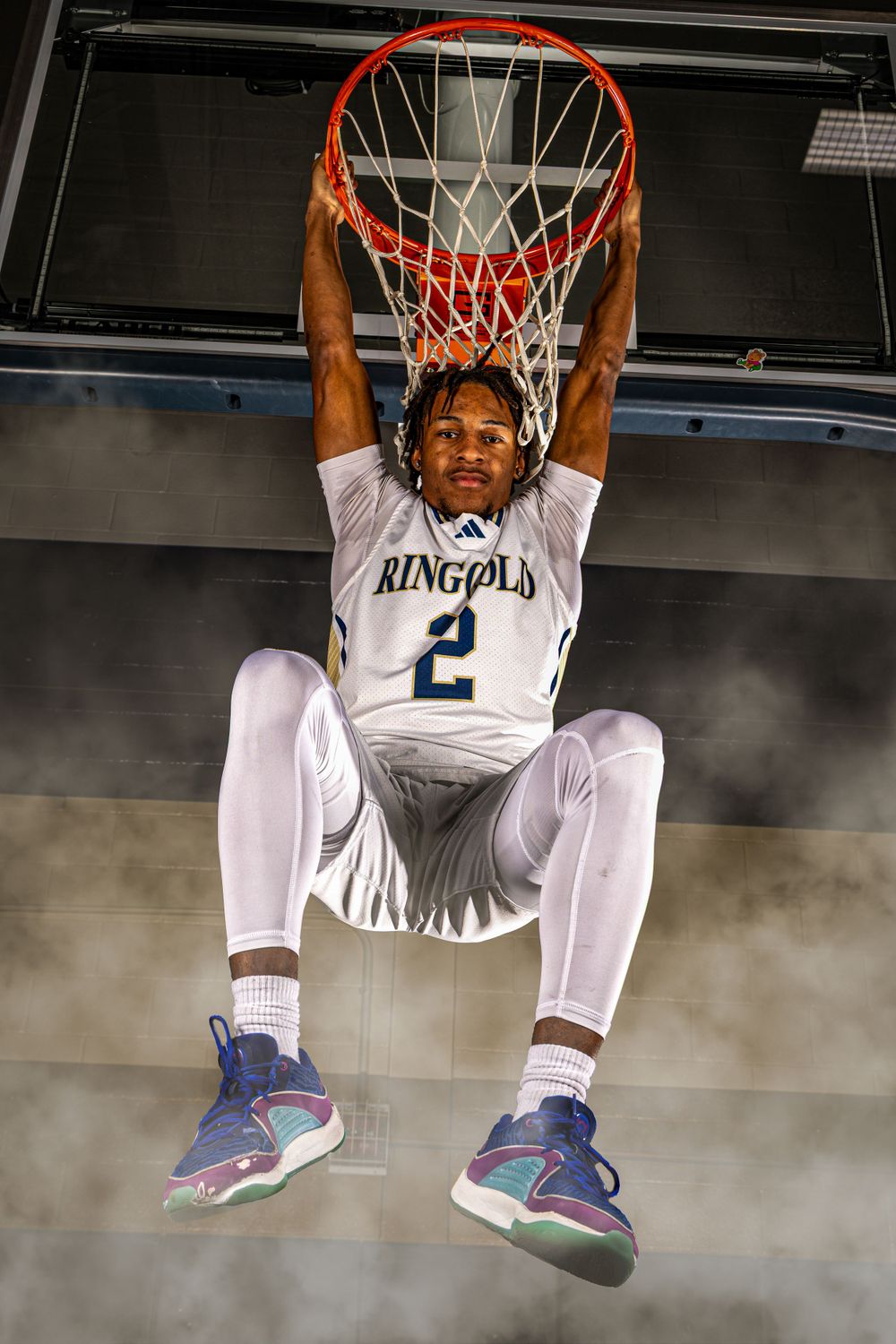 Basketball player in white Kingfold jersey number 2 hangs from rim after slam dunk in smoky gymnasium atmosphere.