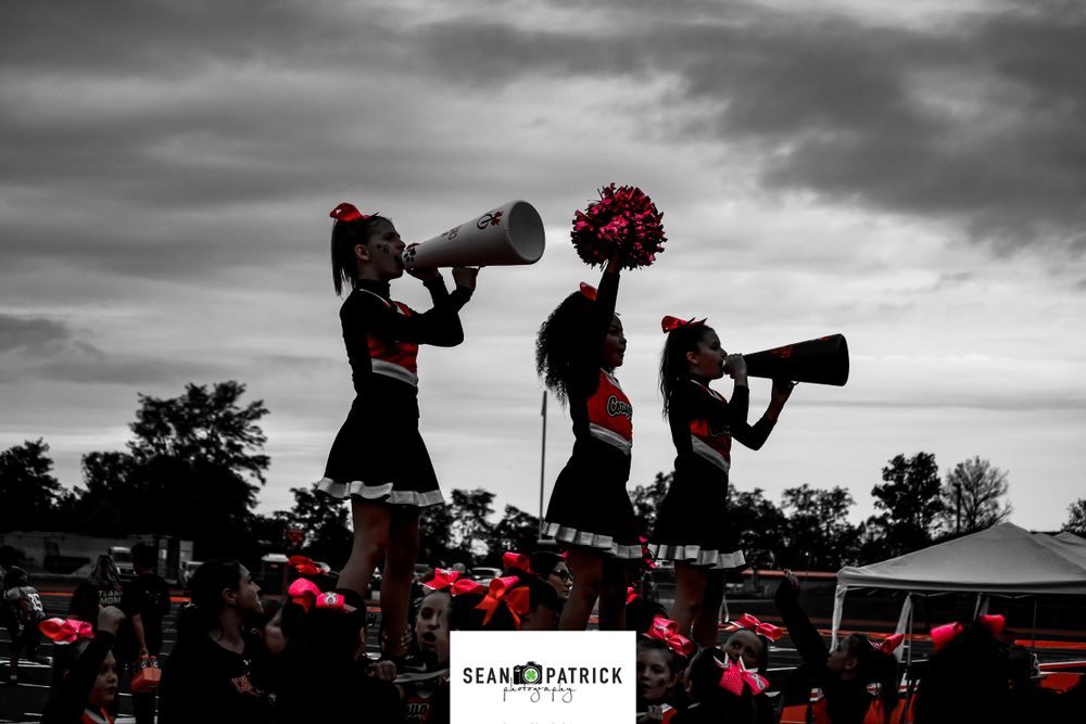 Silhouette of cheerleaders with megaphones against dramatic sky with red accents.