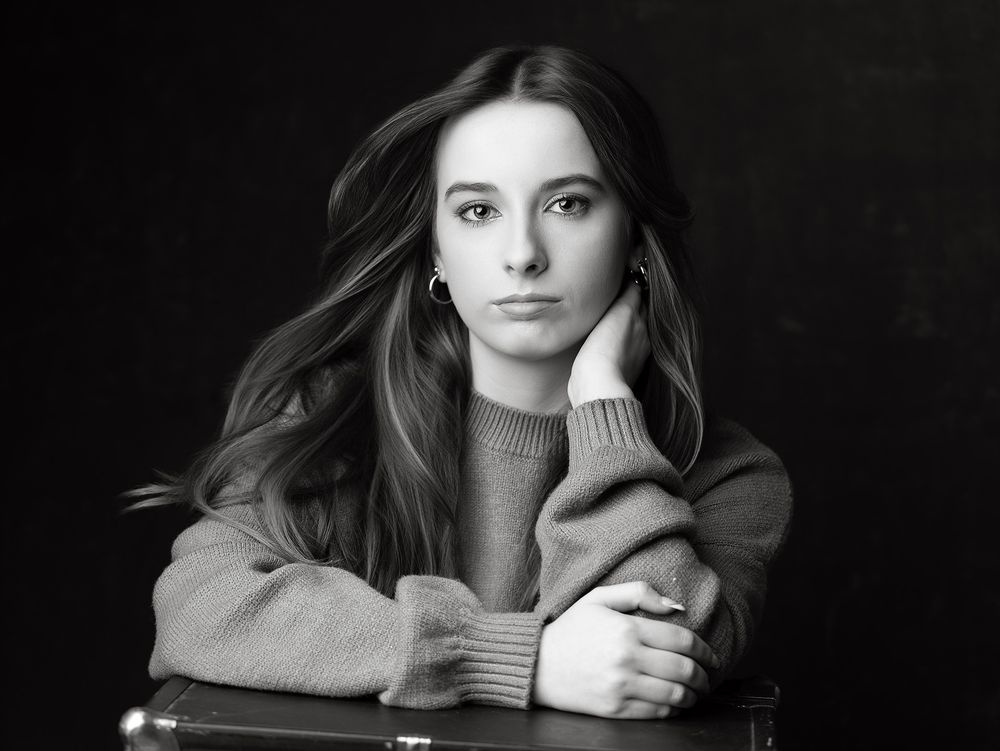 Black and white portrait of a young woman with long hair resting her chin on her hand at a table.
