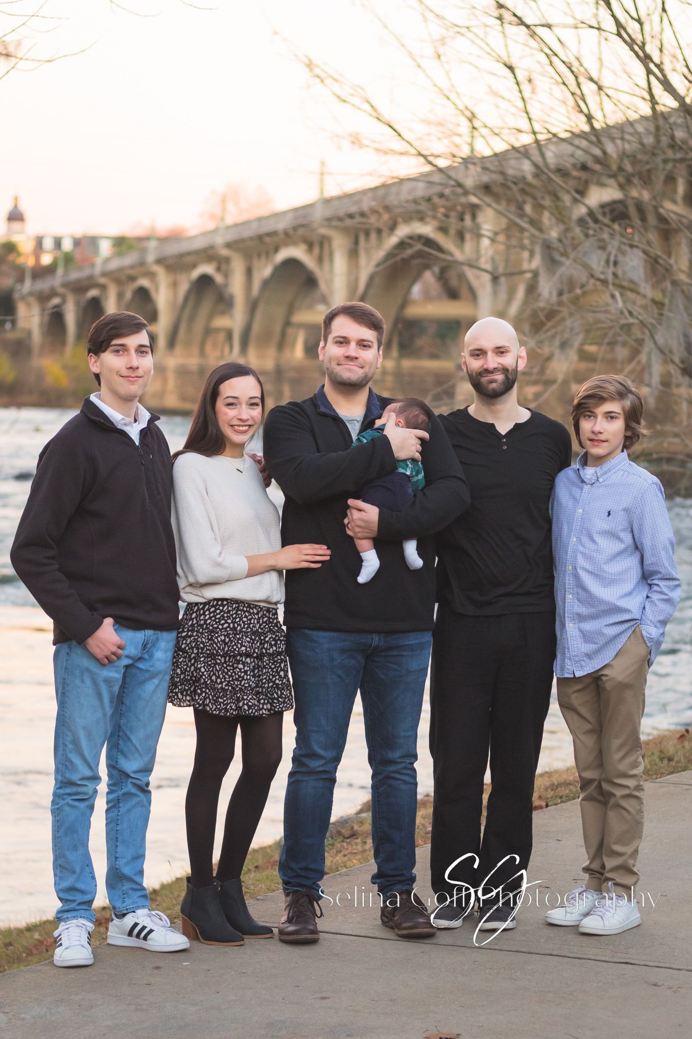 A group poses together for a portrait by a bridge at sunset.
