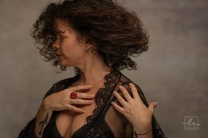 Dramatic side profile of someone with wild curly dark hair wearing black lace in a moody studio portrait.