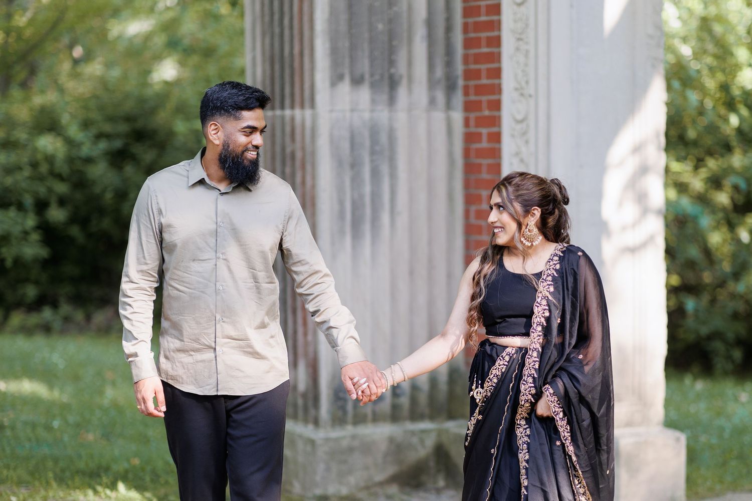 Engaged couple holding hands and smiling while walking in a garden setting.