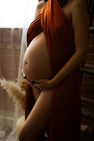During a Fort Worth maternity boudoir session, a mother holds her belly.