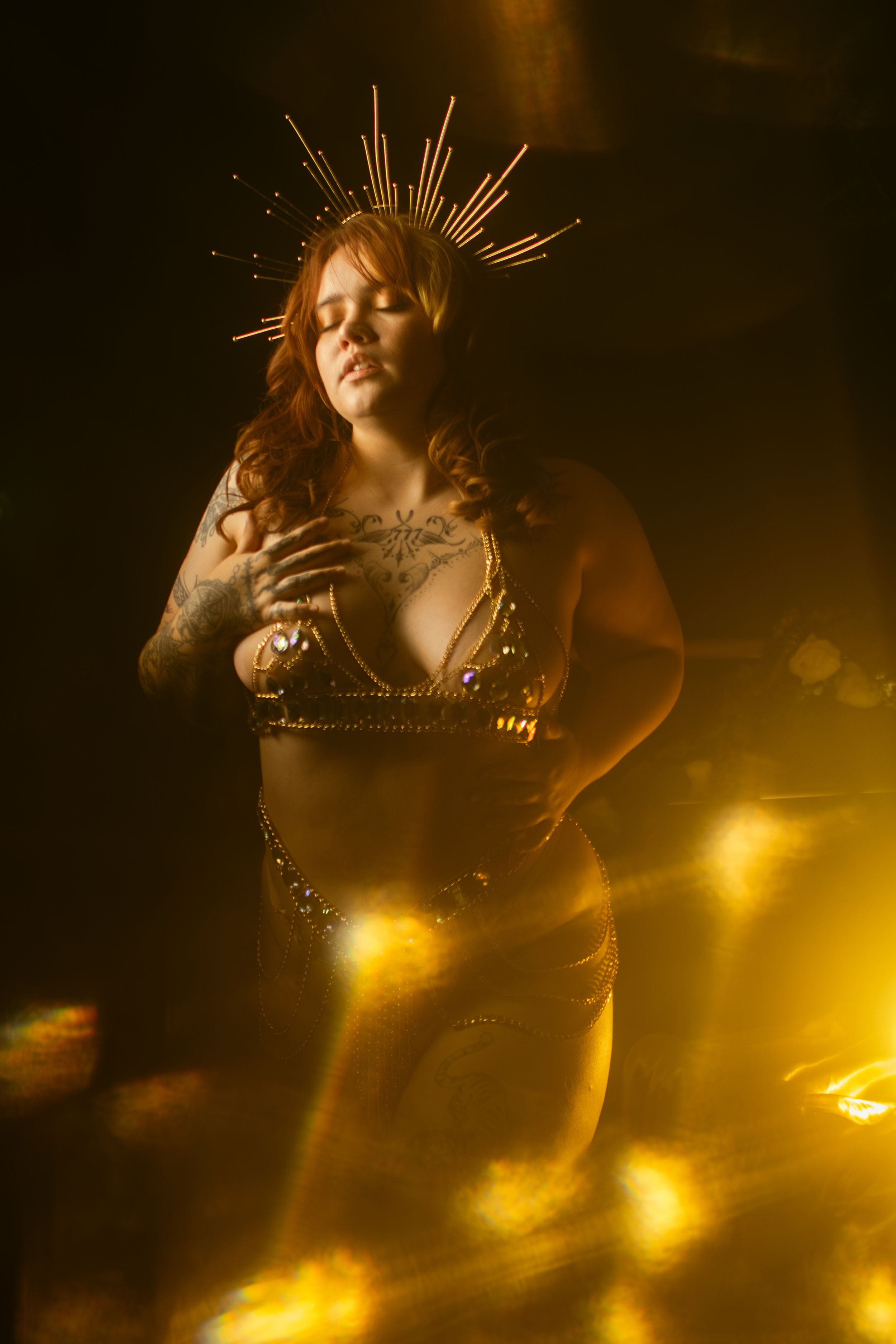 Artistic fantasy boudoir photo in golden light with spiky crown headpiece and dramatic shadows creating ethereal atmosphere.