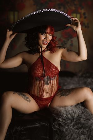 Boudoir photo featuring red lace lingerie and a large black hat against a dark background with festive decor.