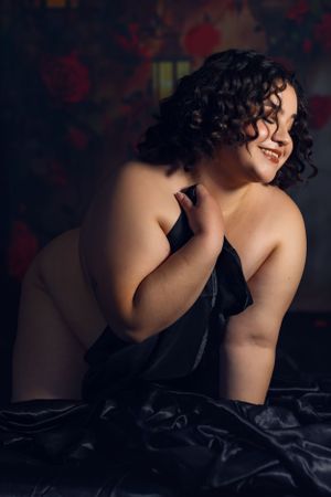 A boudoir photo featuring curly dark hair and bare shoulders against a moody dark background with red accents in Fort Worth, Texas.