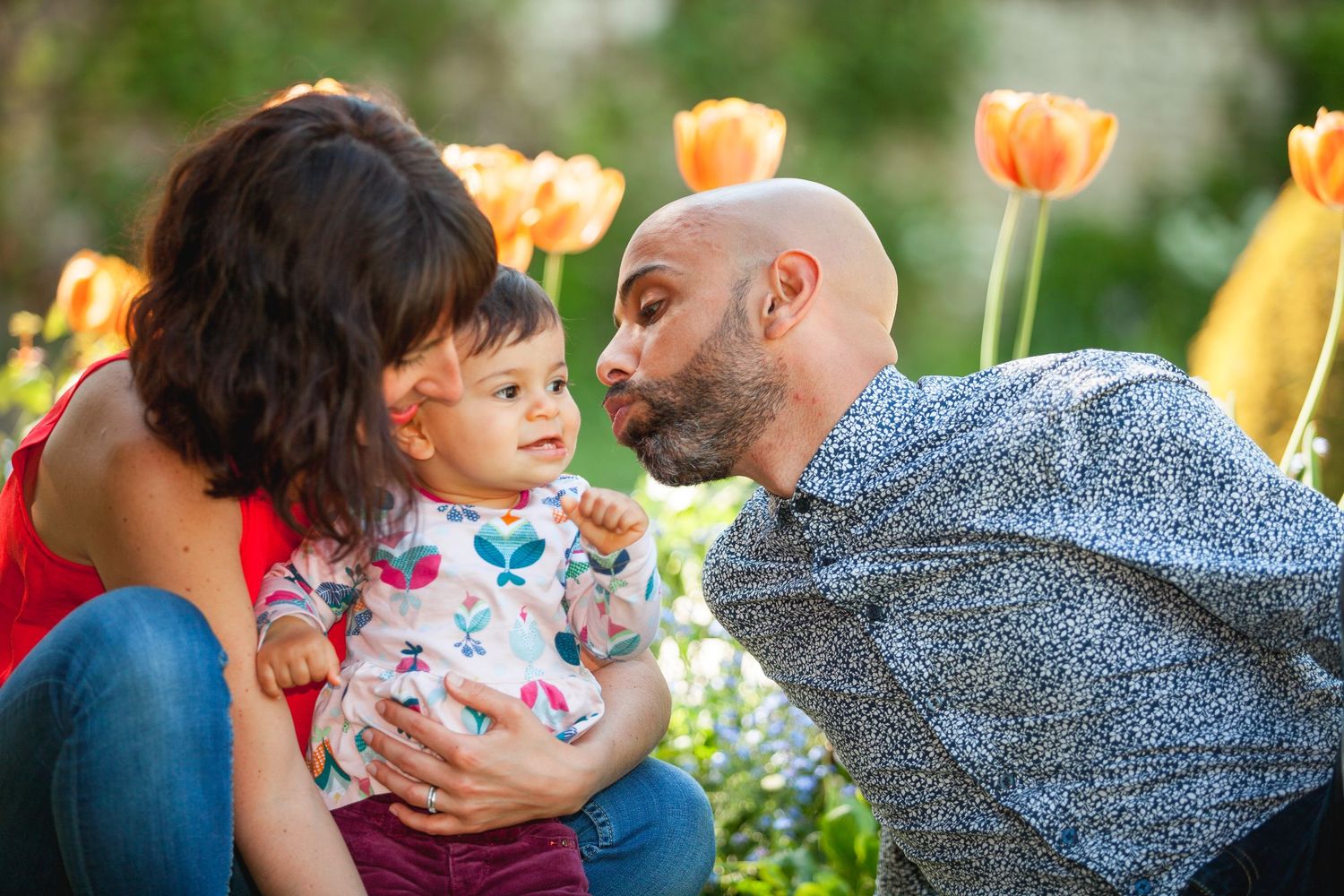 Un papa qui se penche vers le bébé qui est dans les bras de maman pour lui faire un bisou