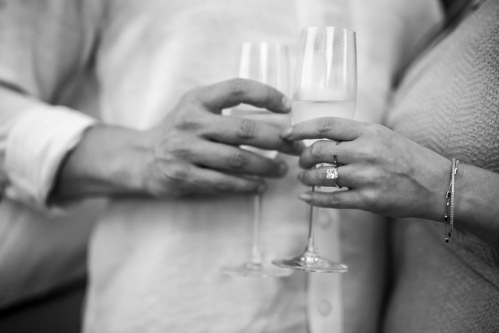 Close-up black and white photo of champagne glasses and engagement ring.