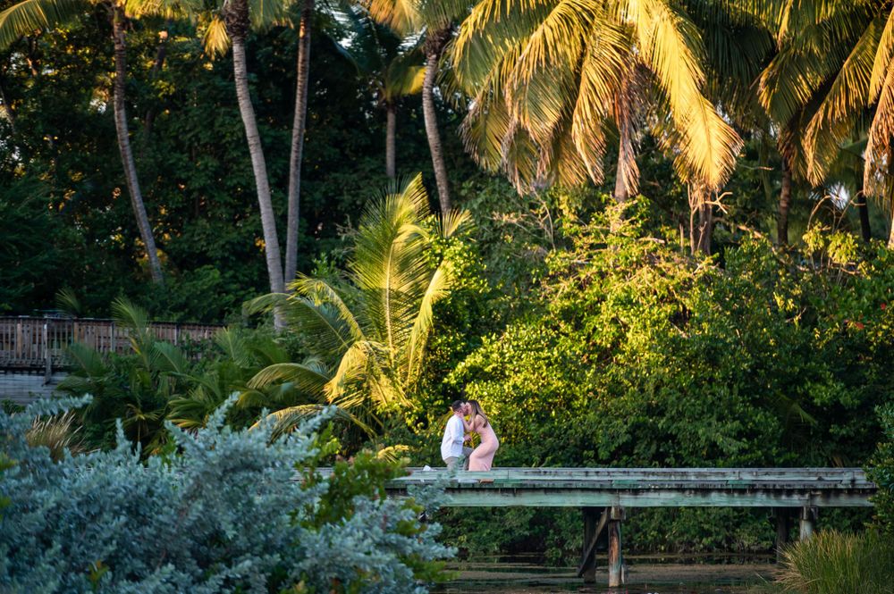 Tropical garden engagement photo with palm trees and lush greenery at sunset.