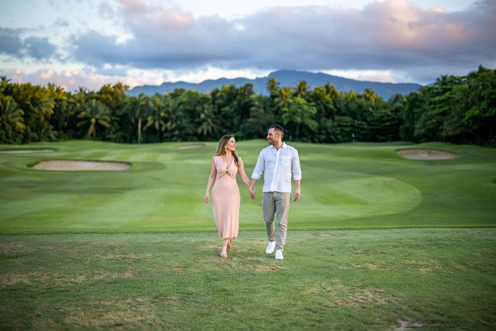 Couple walking hand in hand on scenic golf course with mountain backdrop.